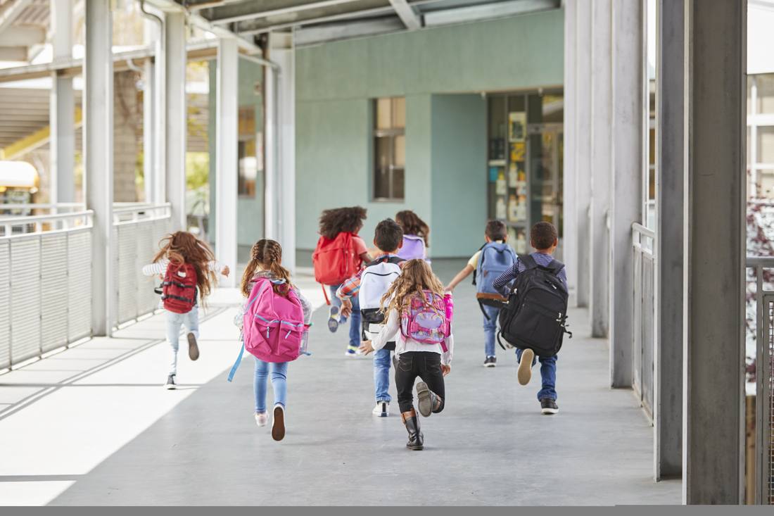 Elementary kids running down a school walkway with backpacks